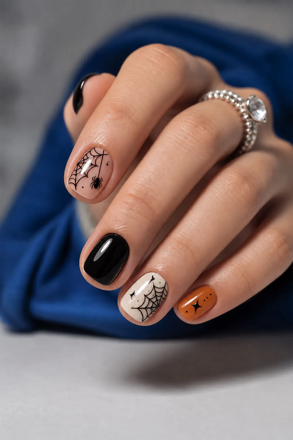 Short halloween nails in black with a white spiderweb and orange accent