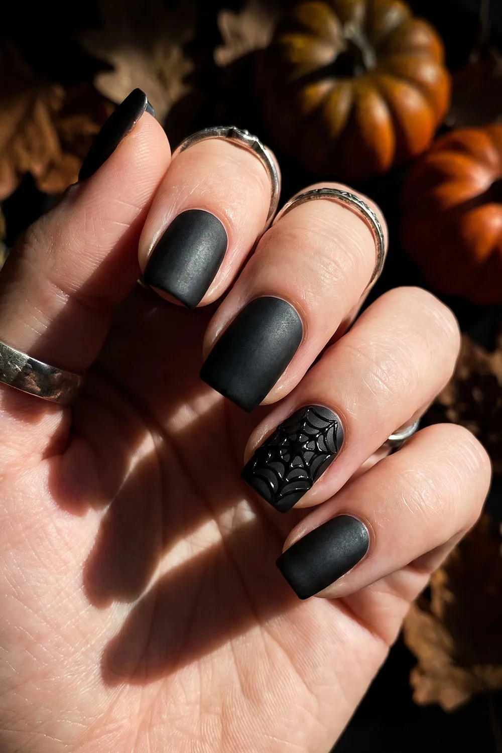Matte black short halloween nails with a spiderweb accent nail